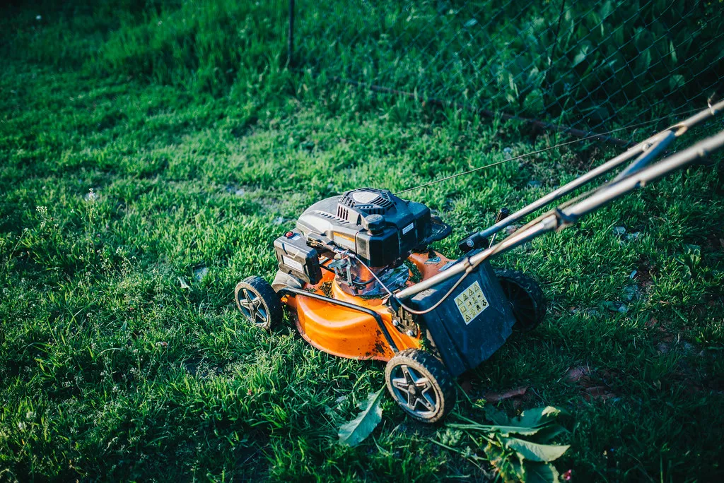 A gas push mower sitting on freshly cut green grass in a residential backyard. A gas push mower sitting on freshly cut green grass in a residential backyard.